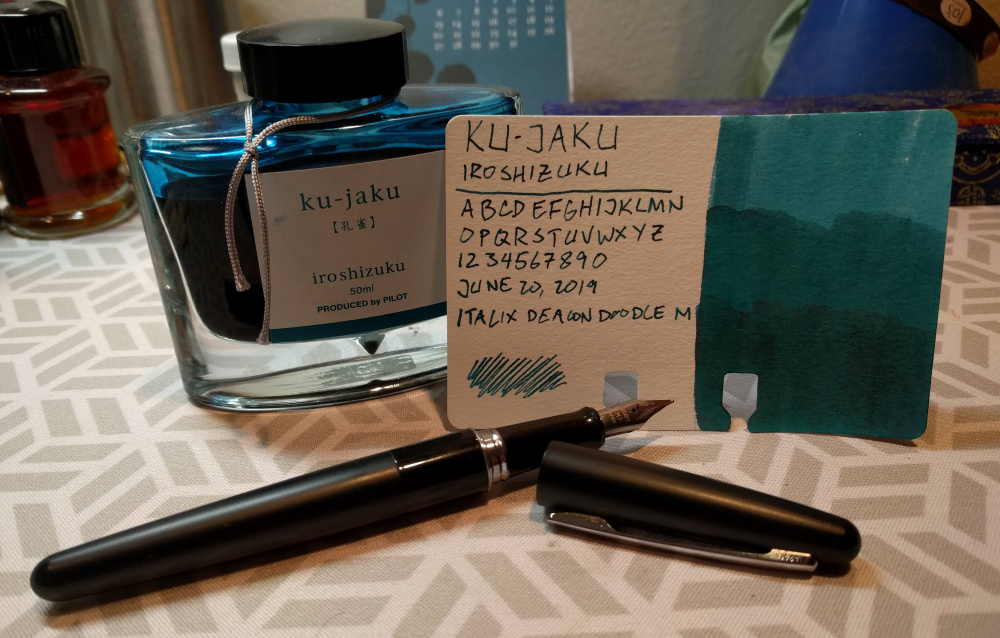 a bottle of turquoise ink, a swatch card, and a black fountain pen
